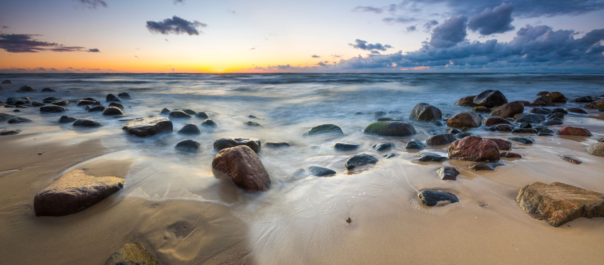 Sonnenuntergang über der Ostsee mit Steinen am Strand; ein Ort des Abschieds und der Erinnerung durch Bestattung Hinz.