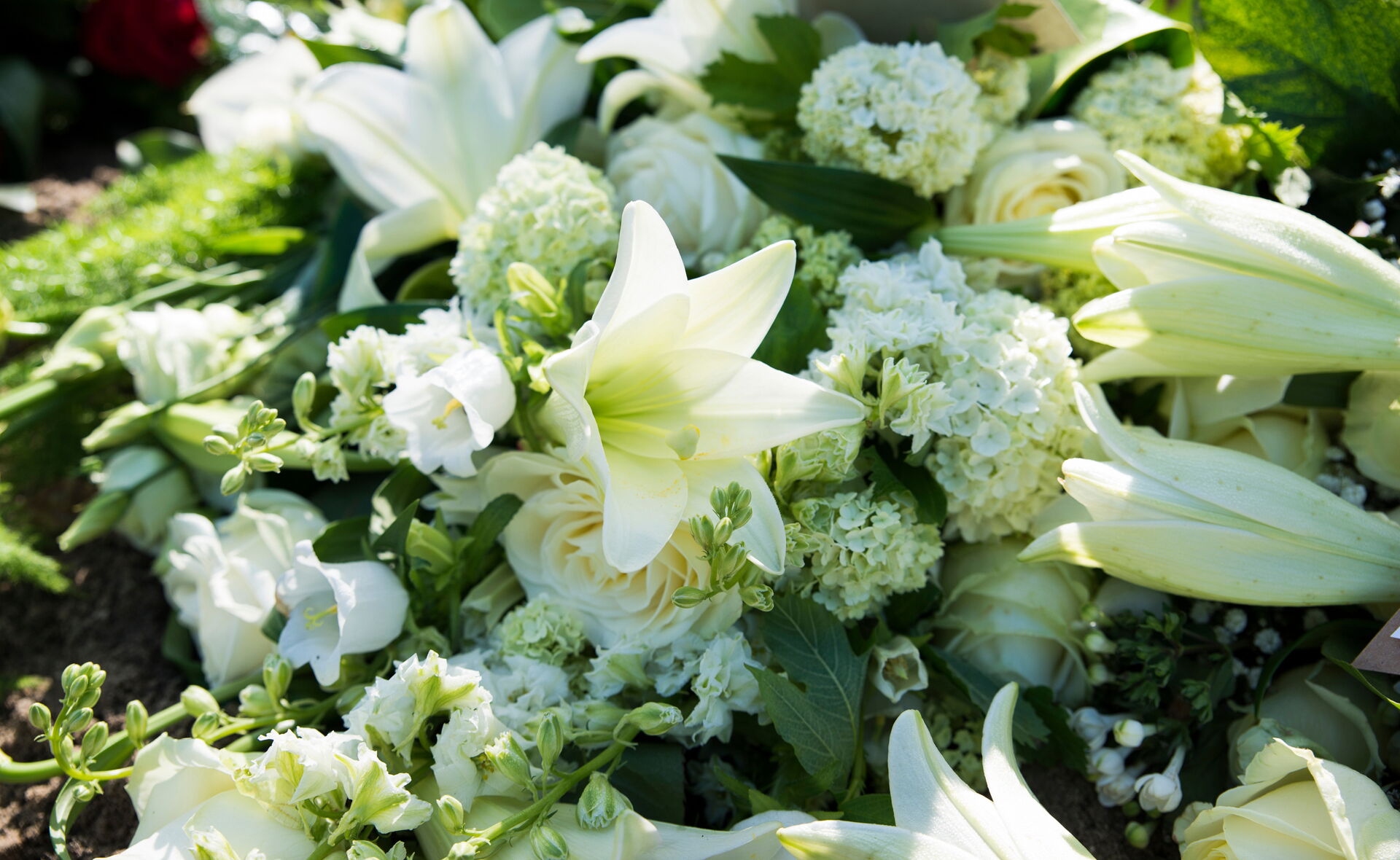 Ein elegantes, weißes Trauergesteck mit Lilien und Rosen; würdevolle Trauerfloristik von Bestattung Eva-Maria Hinz in Bautzen.